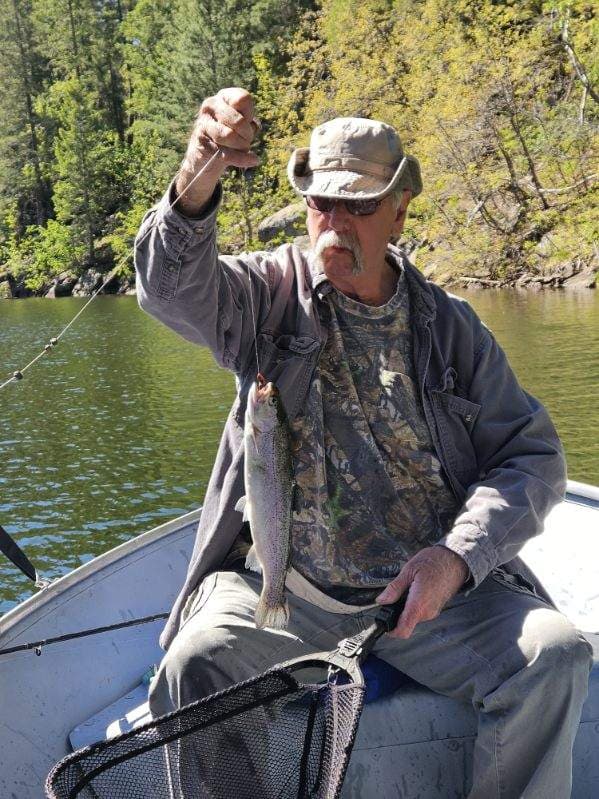 Fisherman with a mustache holds up a caught trout on a line from a boat.